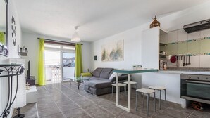 Una cocina moderna con horno integrado, un comedor con mesa de vidrio y un sofá gris.