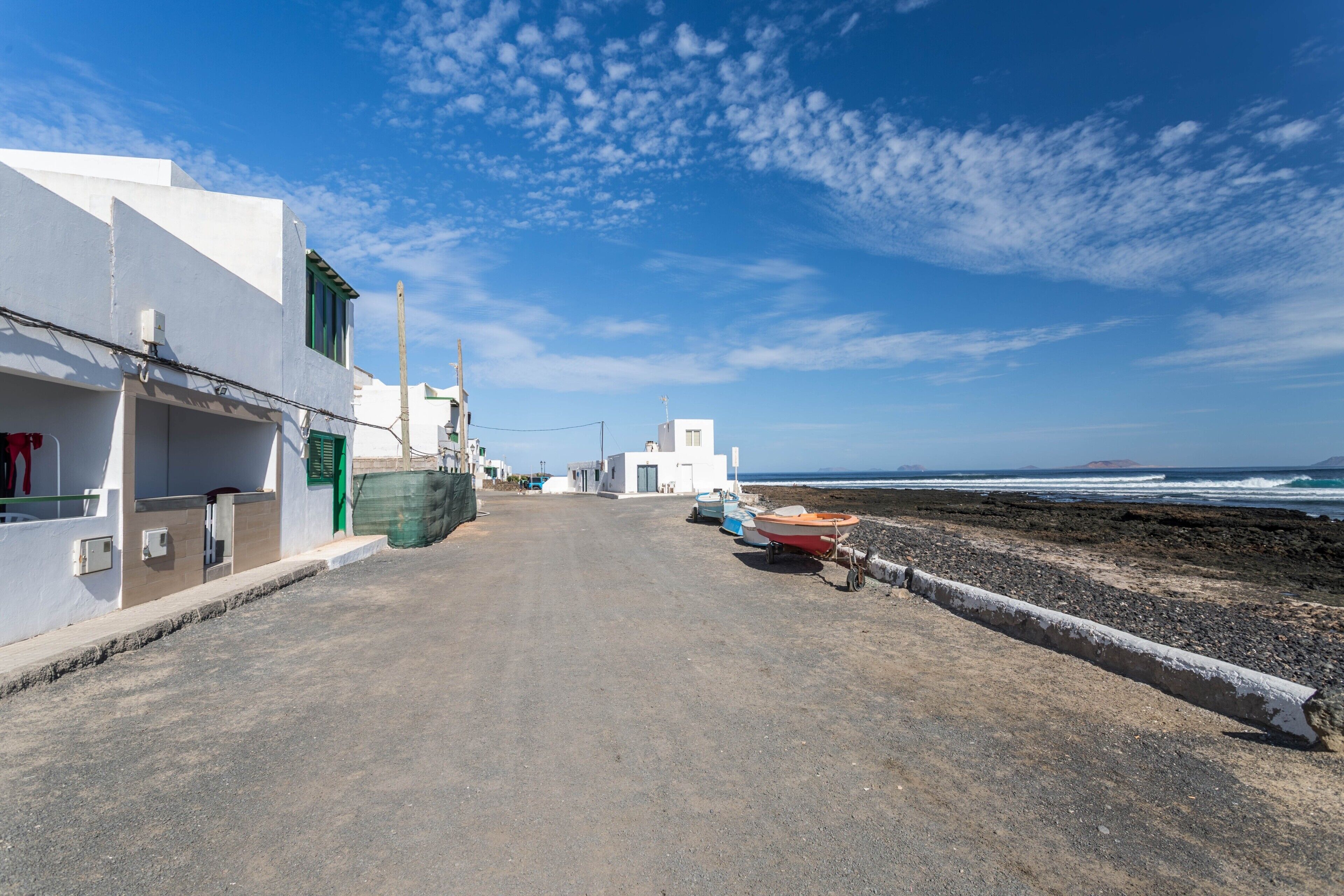 A coastal street with buildings, a road, and boats by the beach.