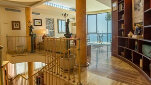 A spacious lobby with a grand staircase, a large bookshelf, and a view of the outdoors. - Villa "Albella" with Sea View, Garden, Terraces, Pool, Sauna, Whirlpool & Gym (San Bartolone de Tirajana)