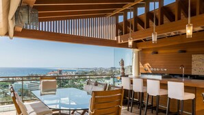 A balcony with a glass table and chairs, a wooden bar area, and a view of the sea. - Villa "Albella" with Sea View, Garden, Terraces, Pool, Sauna, Whirlpool & Gym (San Bartolone de Tirajana)