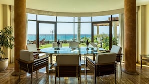 A spacious room with a large glass table surrounded by chairs, large windows offering a view of the sea, and a potted plant. - Villa "Albella" with Sea View, Garden, Terraces, Pool, Sauna, Whirlpool & Gym (San Bartolone de Tirajana)
