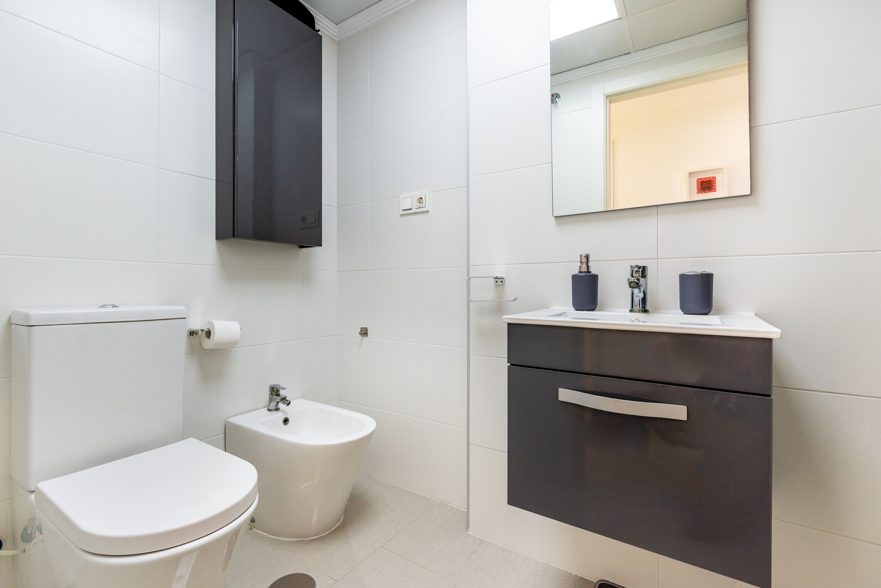 Une salle de bain moderne comprenant des toilettes, un bidet, un meuble-lavabo avec un miroir et un placard.