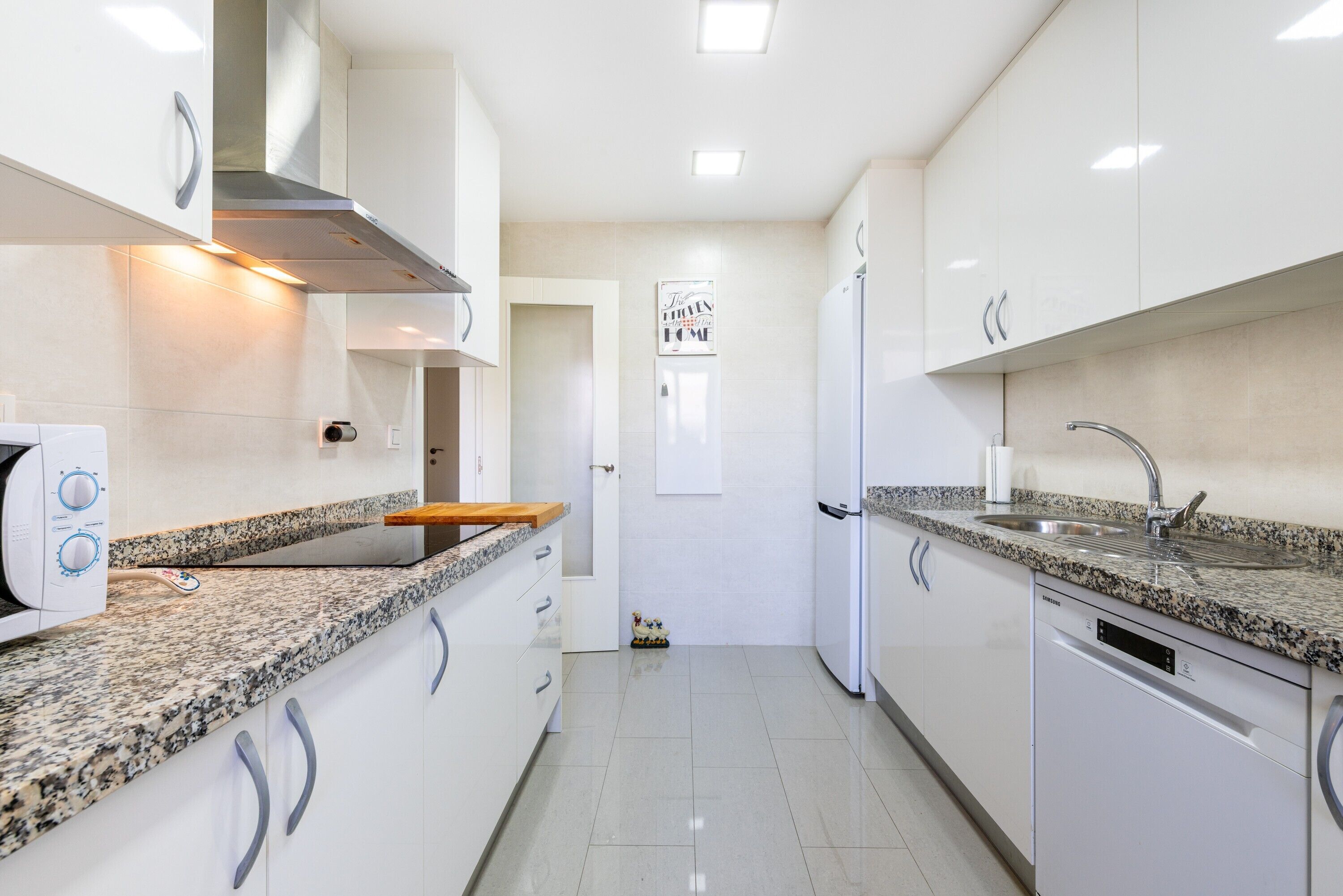 Una cocina moderna con armarios blancos, encimeras de granito y electrodomésticos de acero inoxidable, incluyendo un lavavajillas integrado.