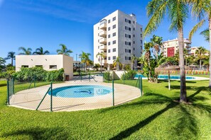 A pool area with a fence, palm trees, and a multi-story building in the background.