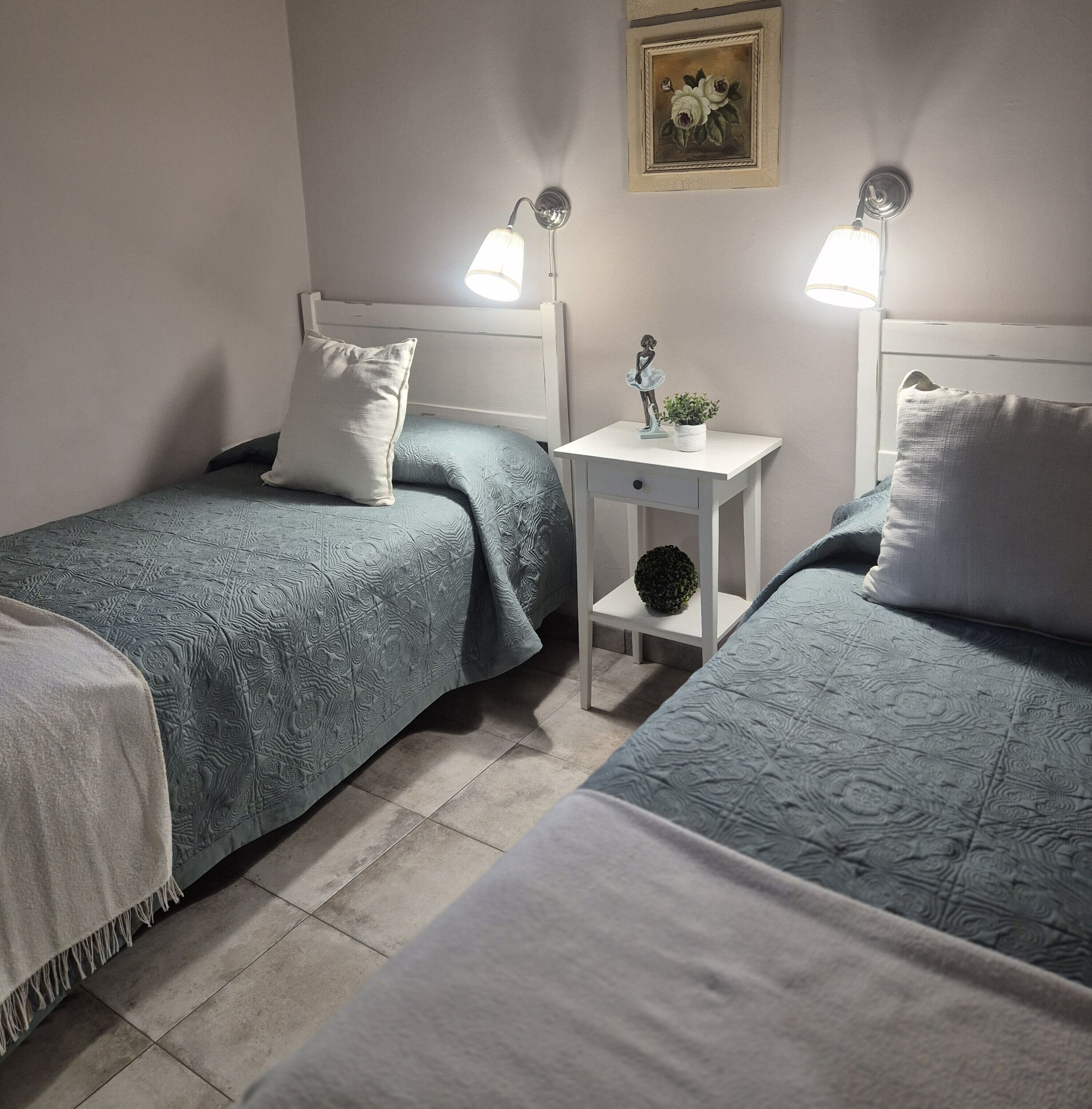 Un dormitorio con dos camas, una mesita de noche, una lámpara de pared y un cuadro enmarcado.