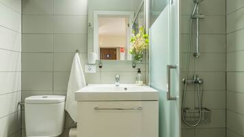 Un baño con inodoro, lavamanos, espejo, ducha y un pequeño florero con flores.