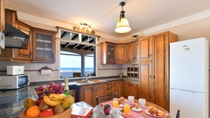 A kitchen with wooden cabinets, a refrigerator, a dining table with breakfast items, and a window with a view. - Villa "Rústica" close to the Beach with Sea and Mountain Views, Pool & Terraces (Matagorda)
