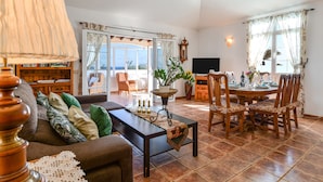 A living room with a sofa, a coffee table, a dining table with chairs, a television, and a view through a glass door. - Villa "Rústica" close to the Beach with Sea and Mountain Views, Pool & Terraces (Matagorda)