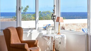 A room with a view of the sea, a checkered armchair, a small table with a lamp, and a chair outside the window. - Villa "Rústica" close to the Beach with Sea and Mountain Views, Pool & Terraces (Matagorda)
