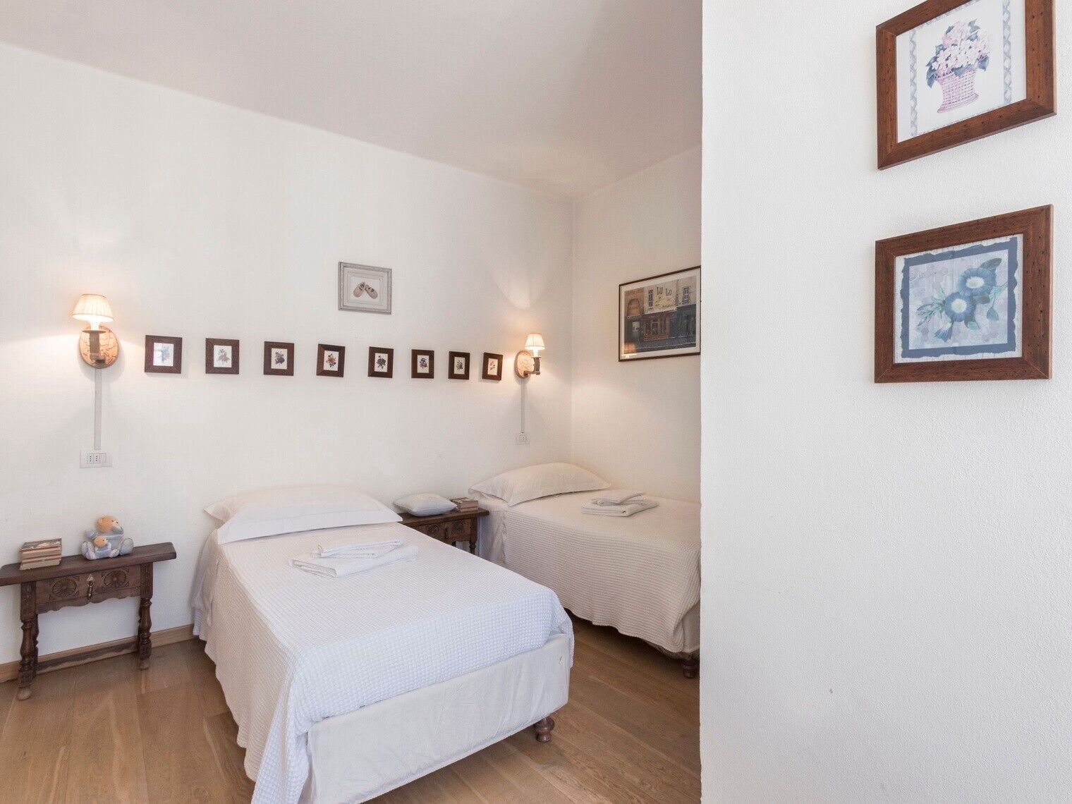 Una habitación de hotel con dos camas, una mesita de noche con lámpara y cuadros en la pared.