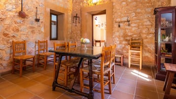 A stone-walled dining area with a wooden table and chairs, a tiled floor, and a wooden cabinet with glass doors.