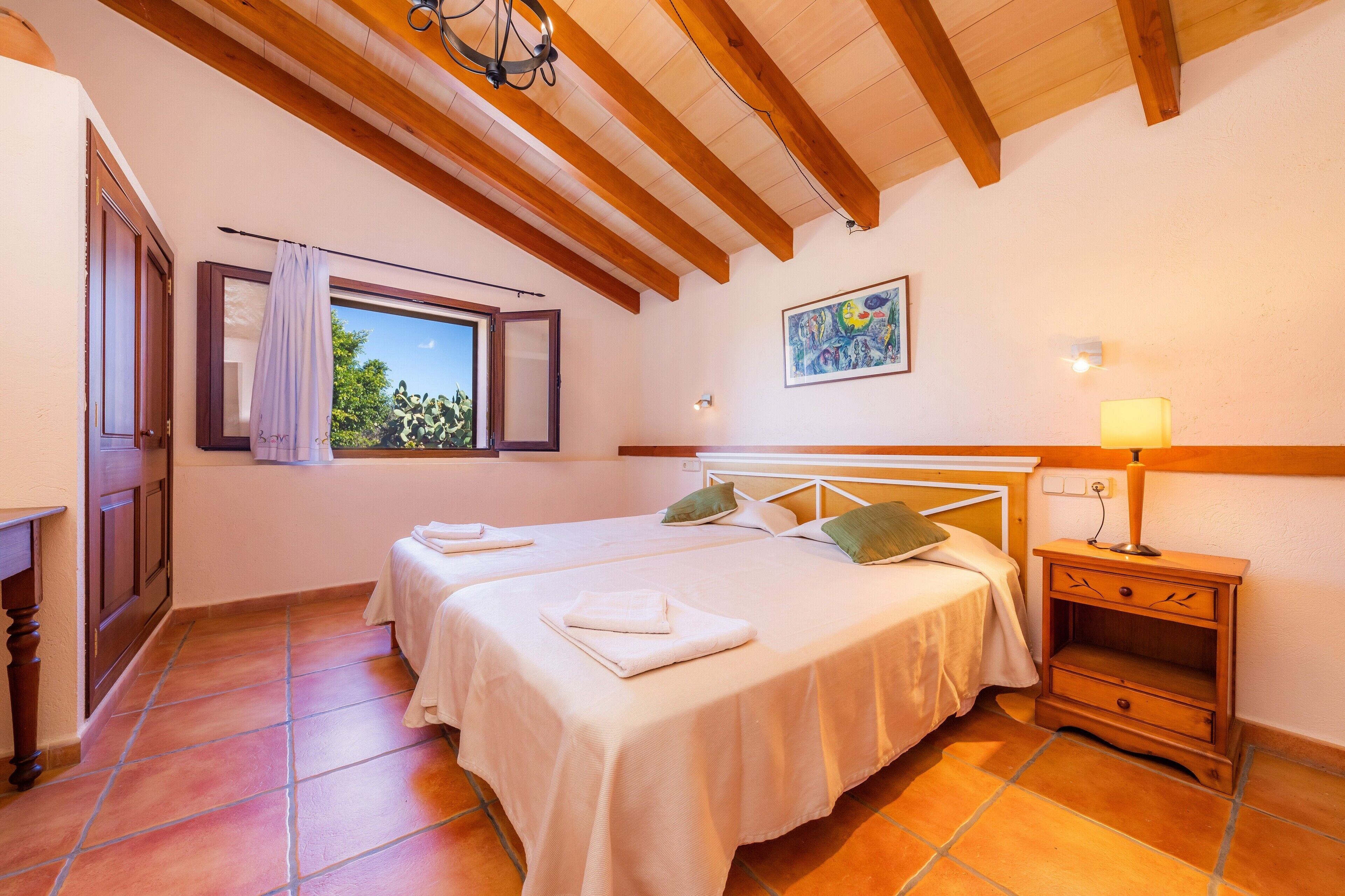 Un dormitorio con dos camas, una mesita de noche, una ventana con cortina, un cuadro en la pared y techo de madera.