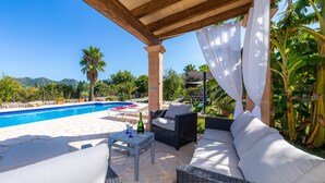 Ein überdachter Außenbereich mit Pool, Korbmöbeln und einem Tisch mit Gläsern und einer Flasche.