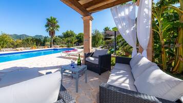 Un espacio al aire libre cubierto con piscina, muebles de mimbre y una mesa con vasos y una botella.