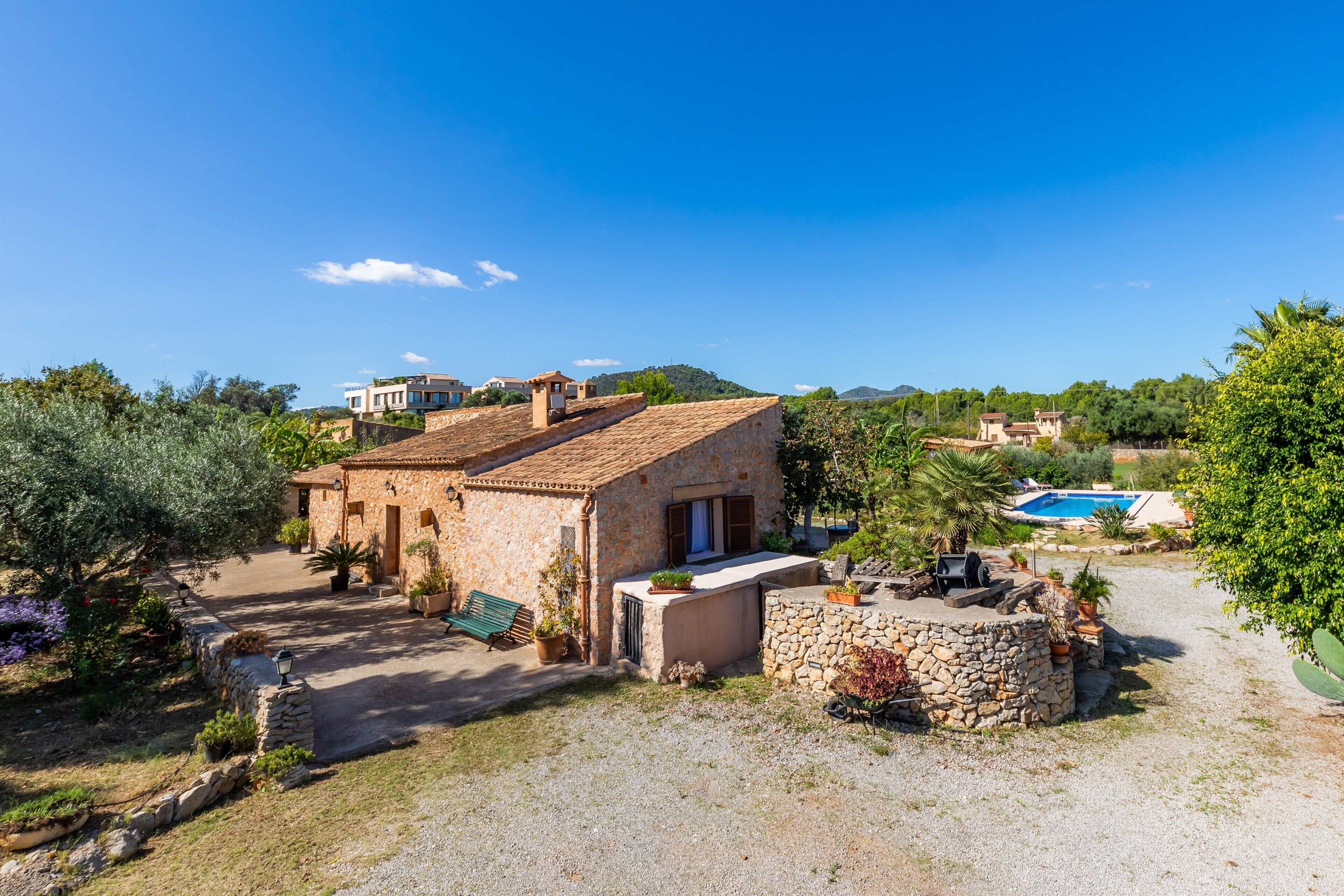 Una casa de piedra con patio, piscina y abundante vegetación alrededor.