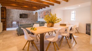A dining area with a wooden table, white chairs, a stone wall, a television, and a fireplace. - Stunning Holiday Home “Finca Rafal” with Garden, Pool, Terraces & WiFi; Parking Available (Son Servera)