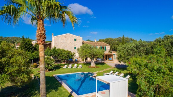 A stone villa with a swimming pool, lounge chairs, and a lush garden.