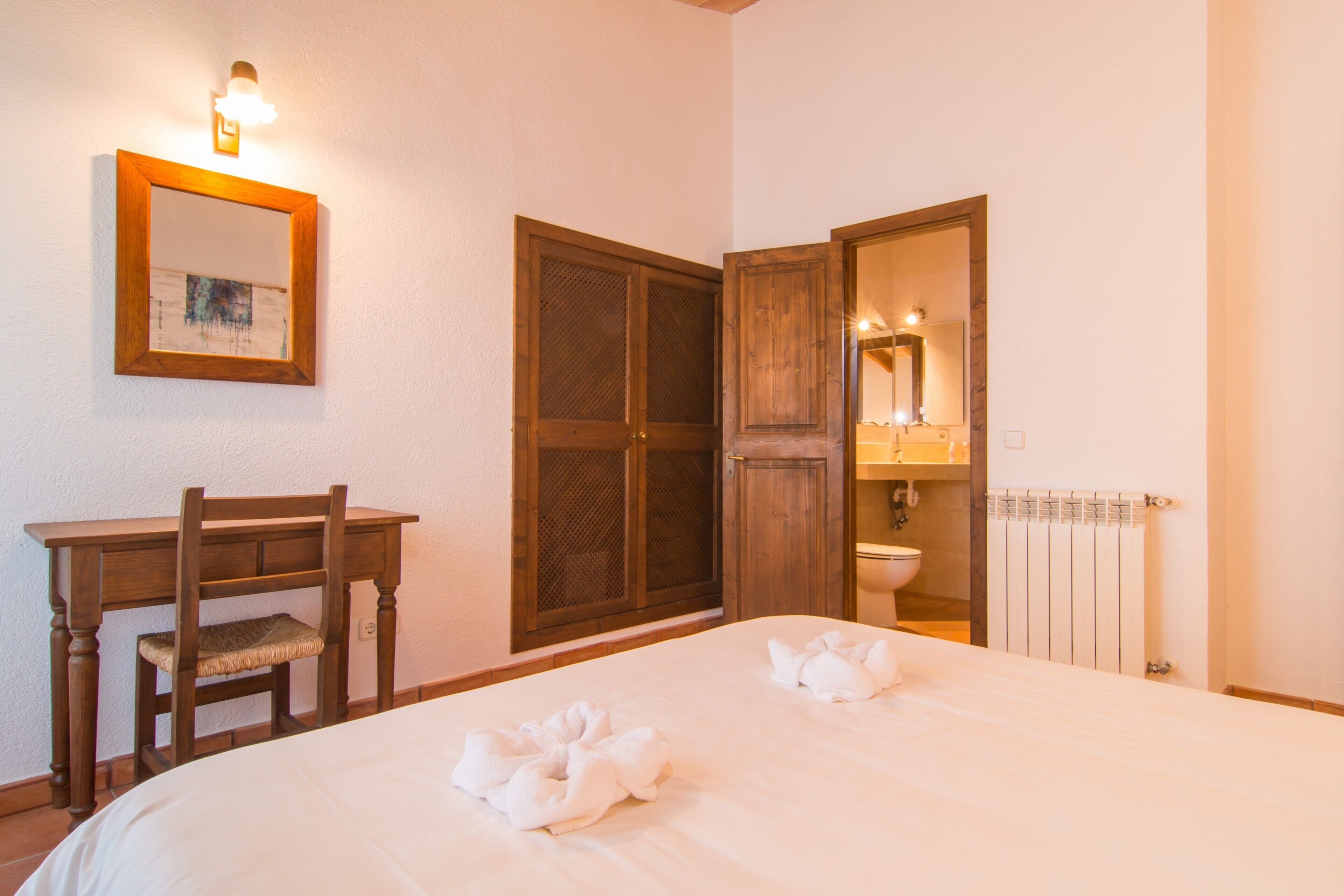 Een slaapkamer met een bed, een bureau, een stoel, een kledingkast en een badkamer met een spiegel en wastafel.