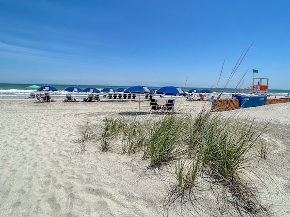 Une plage avec des parasols bleus, des chaises longues et un poste de surveillance pour les sauveteurs.