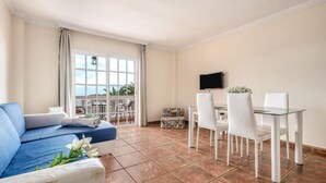 A room with a sofa, dining table, chairs, a TV, and a balcony with a view.