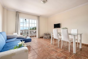 A room with a sofa, dining table, chairs, a TV, and a balcony with a view. - Holiday Apartment “Carla 1A” in Playa San Juan with Sea and Mountain Views (Playa San Juan)