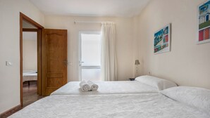 A hotel room with a large bed, a wooden door, a white curtain, and a painting on the wall.