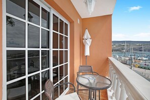 Un balcón con puerta de vidrio, una mesa, sillas y vista hacia un puerto deportivo.