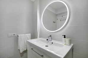 Un baño con un lavabo blanco, un espejo con luz, un perchero y un inodoro.