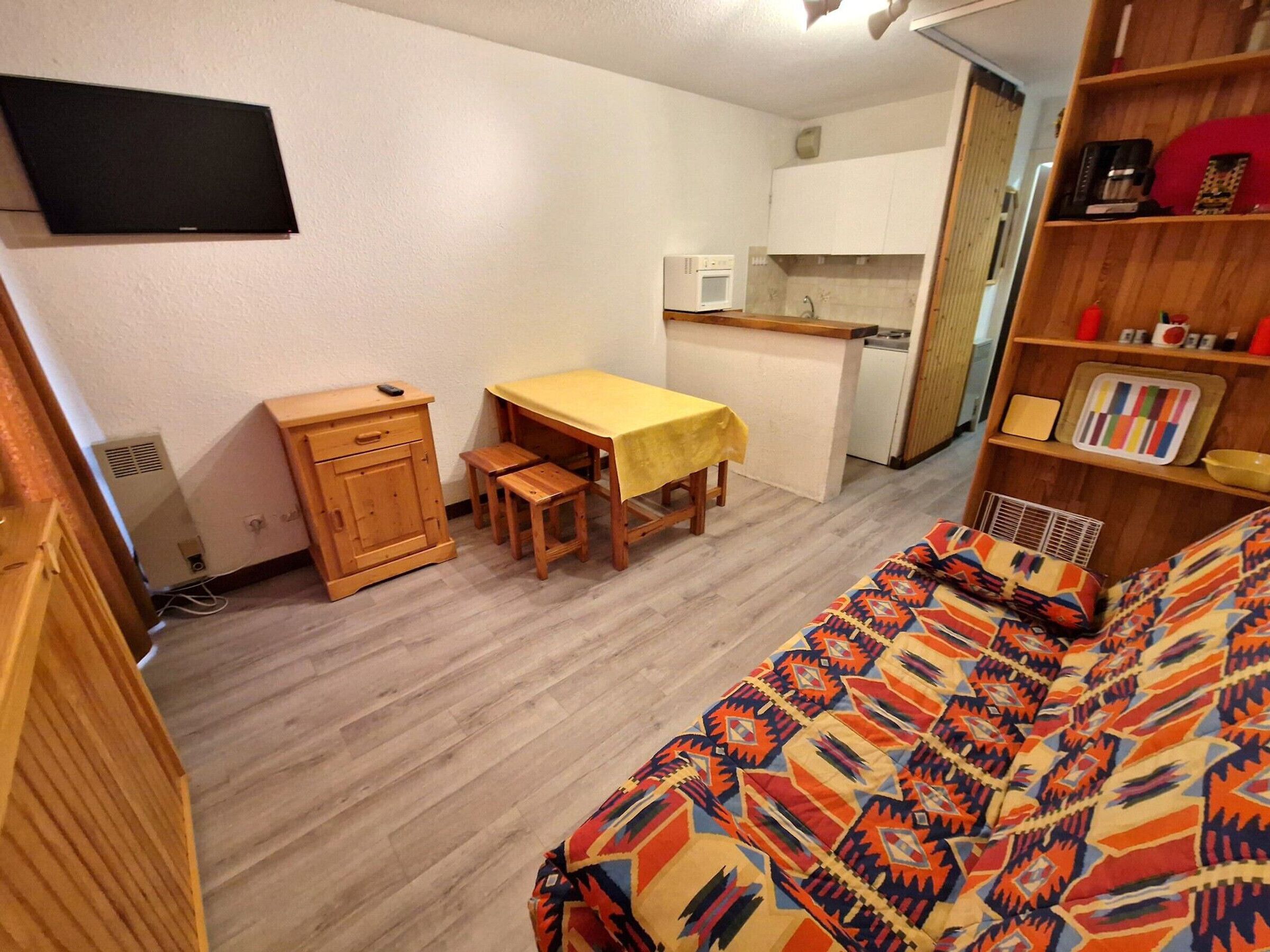 Una habitación compacta con cama, un escritorio pequeño con silla, un microondas y una estantería.