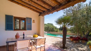 Une terrasse avec une table, des chaises, une bouteille de vin et un saladier de fruits.