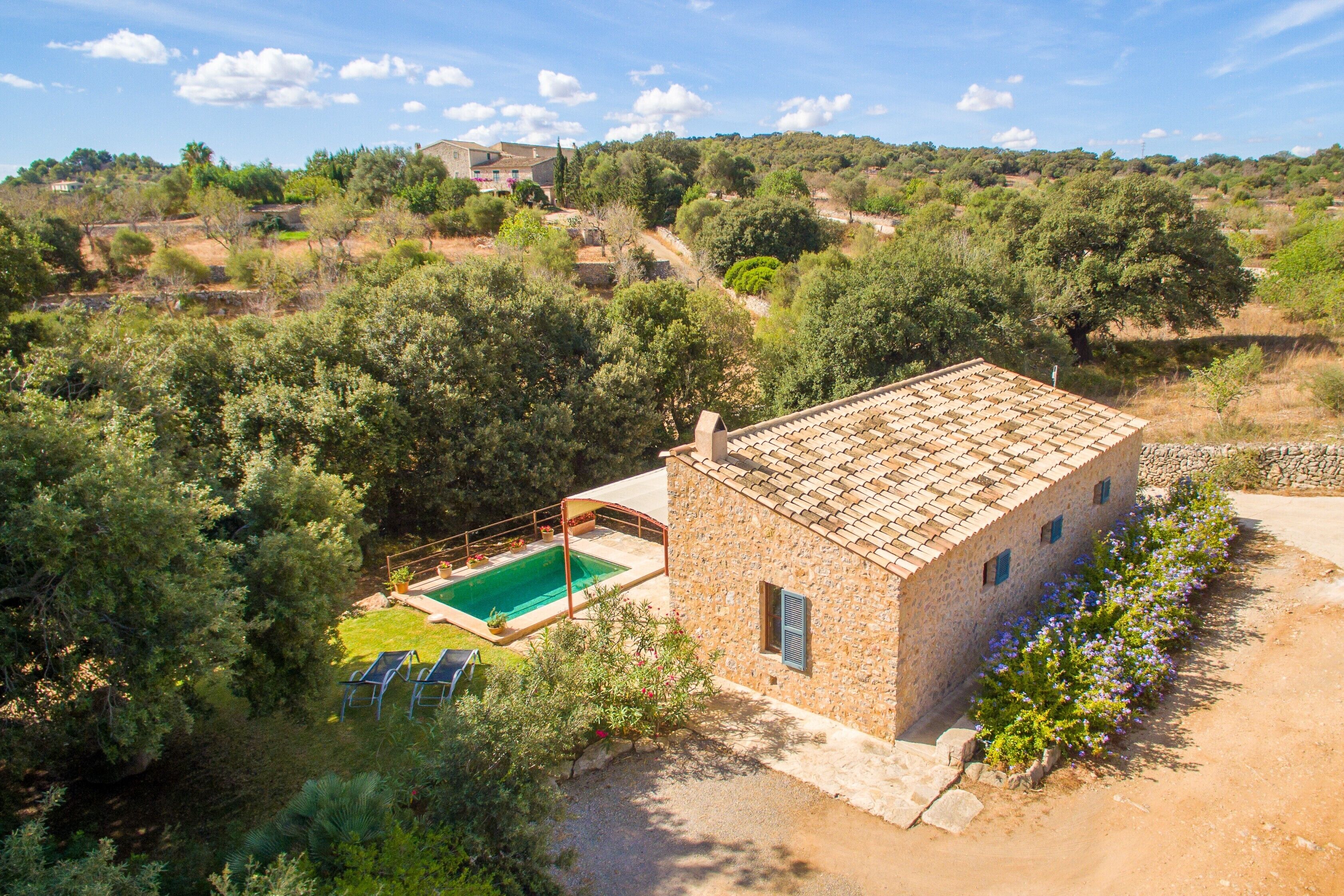 A stone building with a swimming pool, surrounded by trees and a clear sky.
