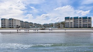 Un hôtel situé en bord de mer, doté de nombreux balcons, d’une plage de sable et de parasols.