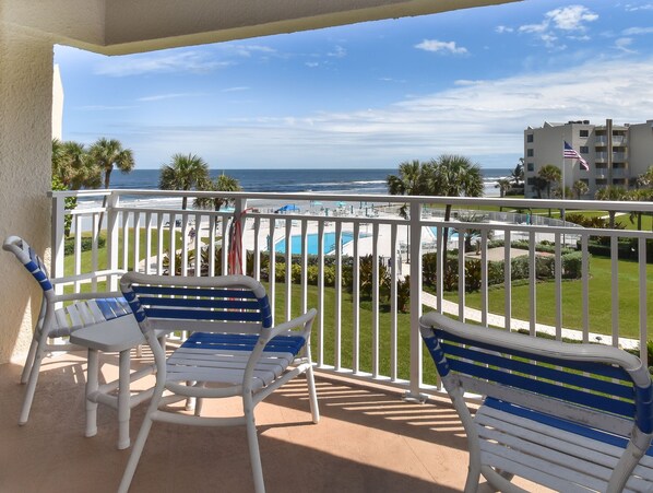 Ein Balkon mit weißen und blauen Stühlen, einem Pool und Blick auf das Meer und Gebäude.