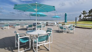 Une terrasse au bord de la plage, dotée de sièges et de parasols, avec vue sur l’océan.