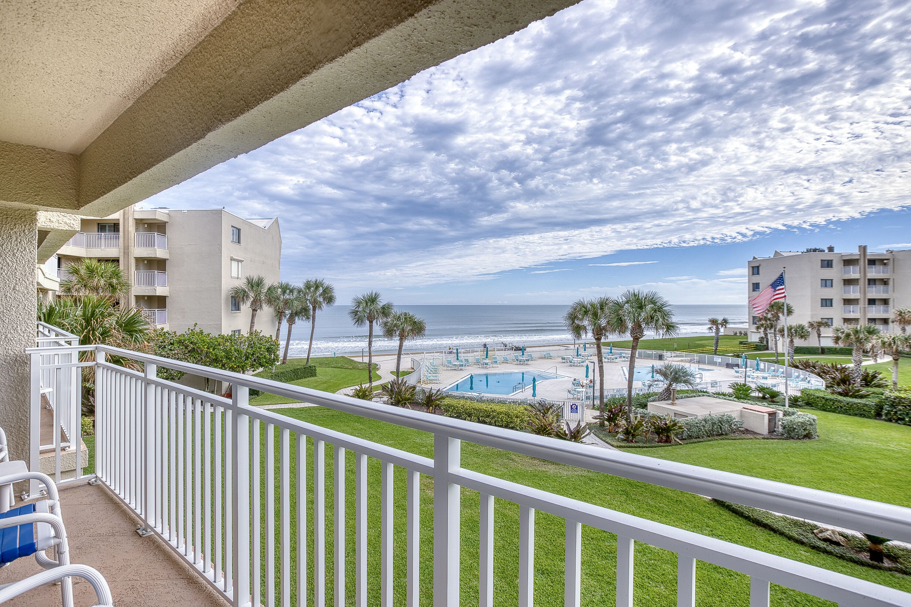 A balcony with a view of a pool area, palm trees, and a beach.