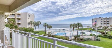 A balcony with a view of a pool area, palm trees, and a beach.