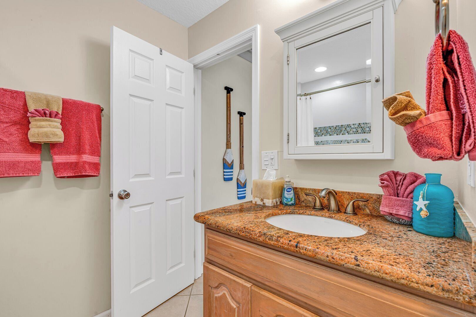 A bathroom with a white door, a granite countertop, a sink, a mirror, and a towel rack with multiple towels.