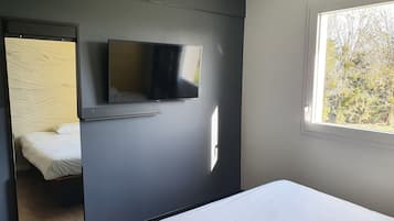 A bedroom with a bed, a wall-mounted TV, and a window with a view of trees.