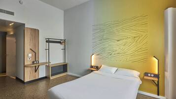 Habitación de hotel con cama, escritorio y lámpara fijada a la pared.