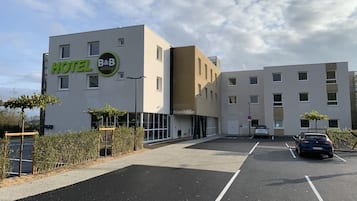 A hotel with a modern design, featuring a prominent 'HOTEL B&B' sign, a parking area, and a building with multiple windows.