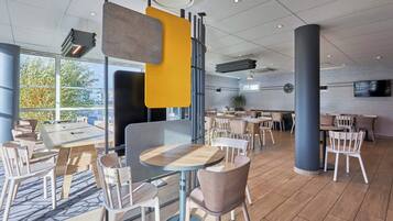 Un comedor moderno con varias mesas y sillas, ventanas amplias y una pared de ladrillo.