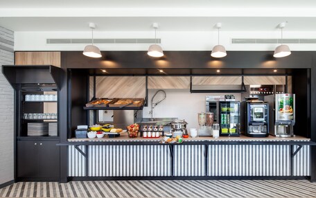 A modern kitchen area with a buffet setup, including a coffee machine, a food display, and various food items.