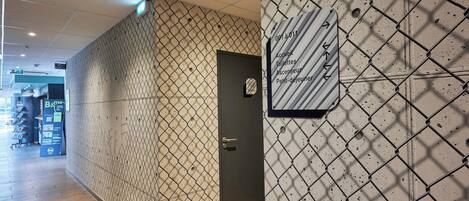A hotel corridor with a chain-link wall, a door with a handle, and a sign with directional arrows.