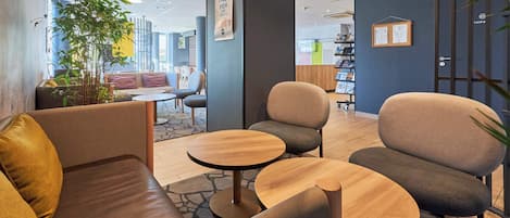 A modern lounge area with leather sofas, round wooden tables, and a large potted plant.