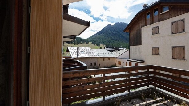 A balcony with wooden railings overlooking a mountainous landscape and traditional buildings.
