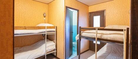 Ein Schlafsaalzimmer mit Etagenbetten, einer Tür zu einem Badezimmer und einem kleinen Fenster.