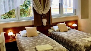 A hotel room with two beds, each with a pillow and a blanket. There are bedside lamps and a window with curtains. - Byczy Rog Noclehy Na Hranici (Kraliky)