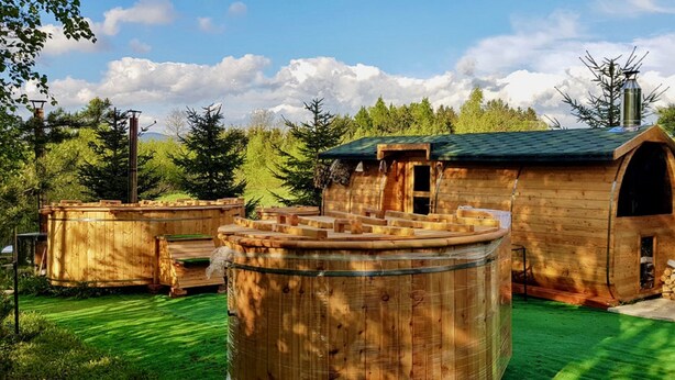 A rustic wooden cabin with a green roof, surrounded by trees and a green lawn. - Byczy Rog Noclehy Na Hranici (Kraliky)