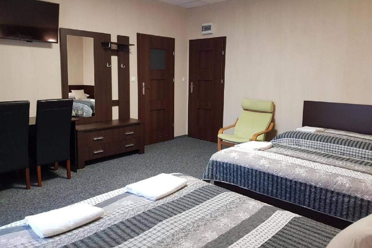 A hotel room with two beds, a desk, a chair, a wardrobe, and a television.