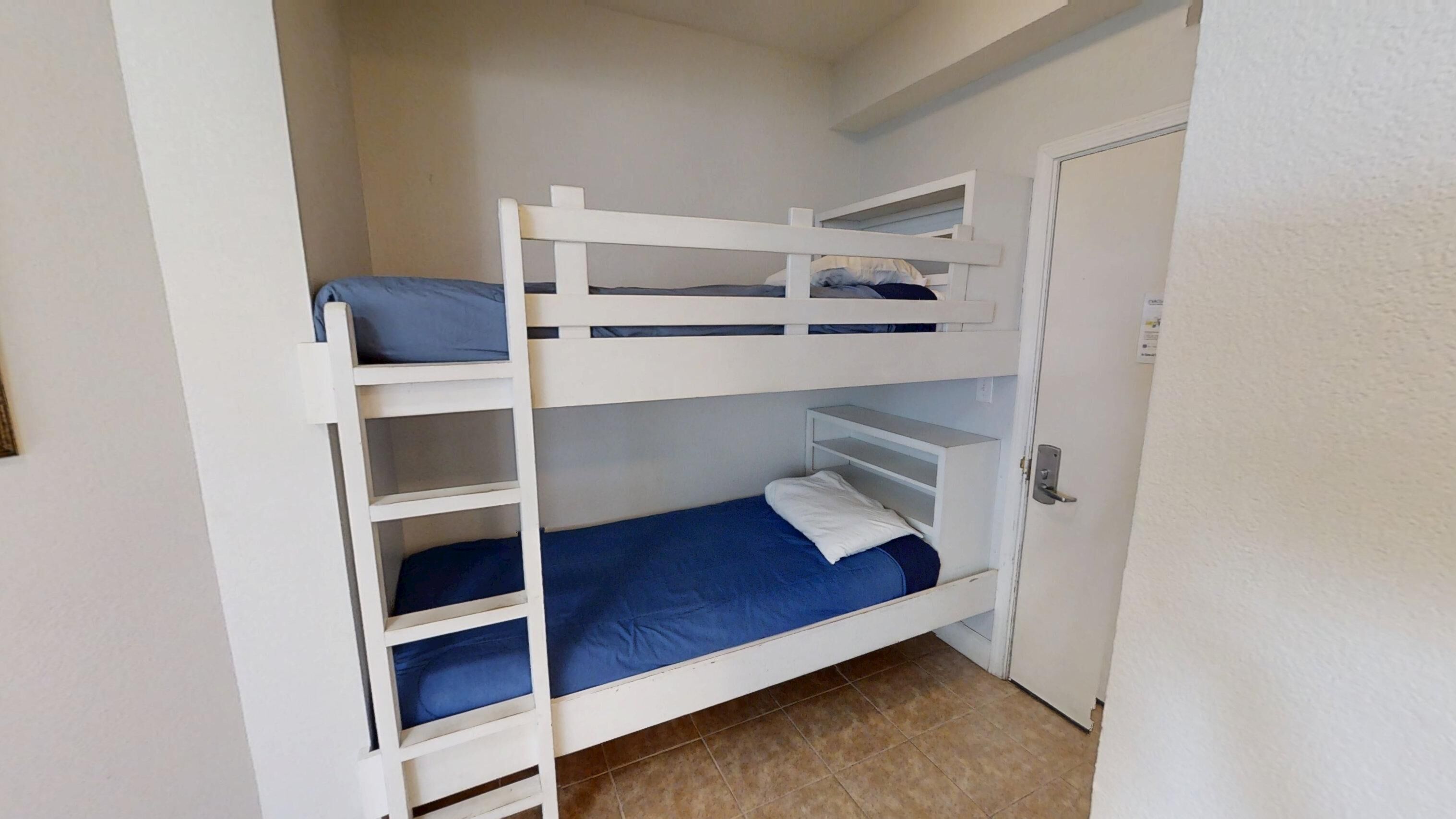 Een slaapkamer met een stapelbed, een deur en een klein plankje.